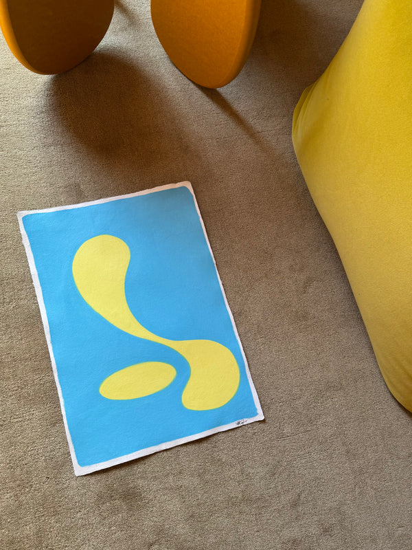 Abstract art print with yellow shapes on a blue background, placed on a textured surface.