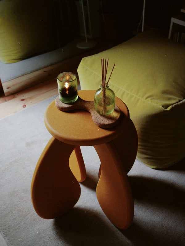 Small wooden table with curved legs with a candle and diffuser on a chunky cork coaster