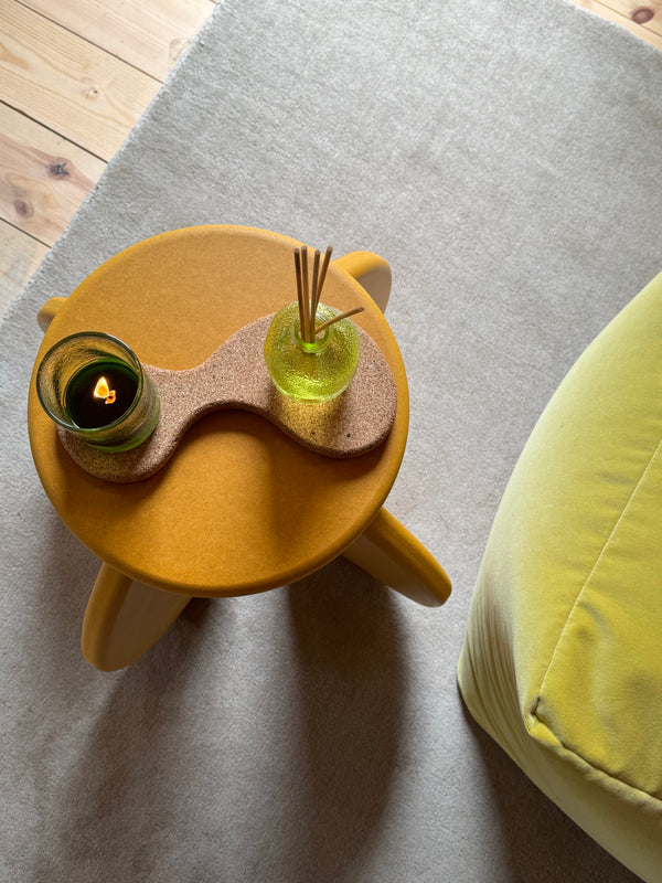 Birds eye view of a round yellow table top with a chunky cork coaster with a diffuser and candle on top.